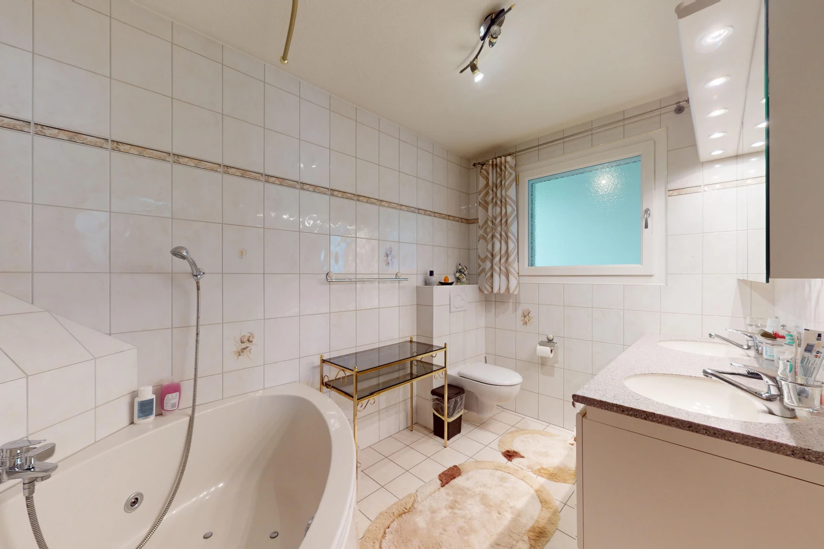 salle de bains avec mur carrelé, vasque, lumière naturelle, et toilettes