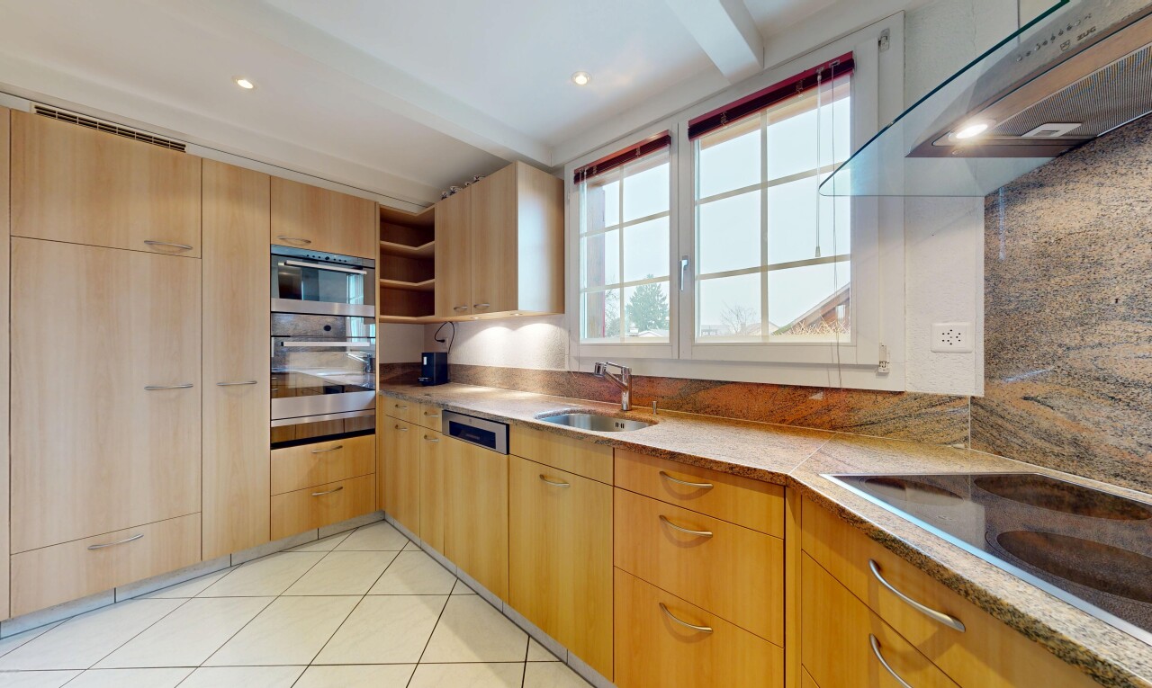 cuisine avec hotte, armoires marron clair, plans de travail en pierre, inside property, et natural light