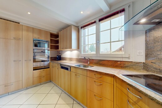cuisine avec hotte, armoires marron clair, plans de travail en pierre, inside property, et natural light