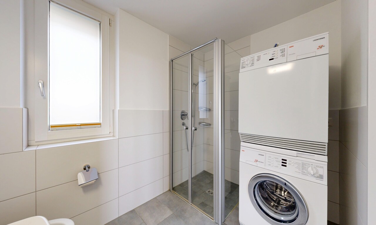 bathroom featuring a stall shower, tile walls, and stacked washer and clothes dryer