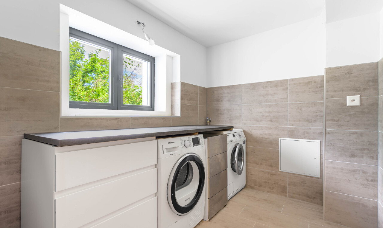 buanderie avec lave-linge et sèche-linge séparés, tile wall, mur en carrelage, inside property, et natural light