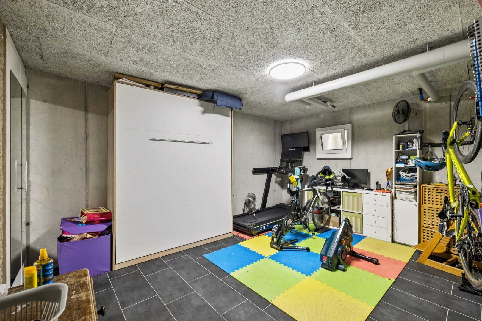 gym avec sous-sol, concrete wall, mur en béton, dark floor, et télévision