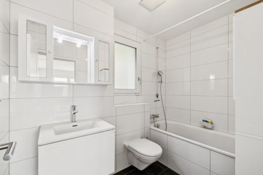 salle de bains avec douche-bain combinés, salle de bain complète, toilette, lavabo (ou coiffeuse selon le contexte), et tile wall