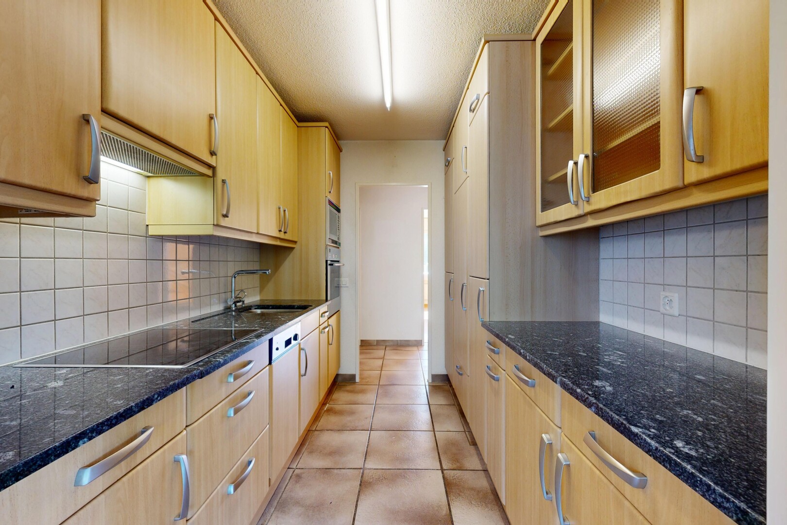 cuisine avec glass insert cabinets, armoires avec insert en verre, dark countertops, light brown cabinets, et armoires marron clair