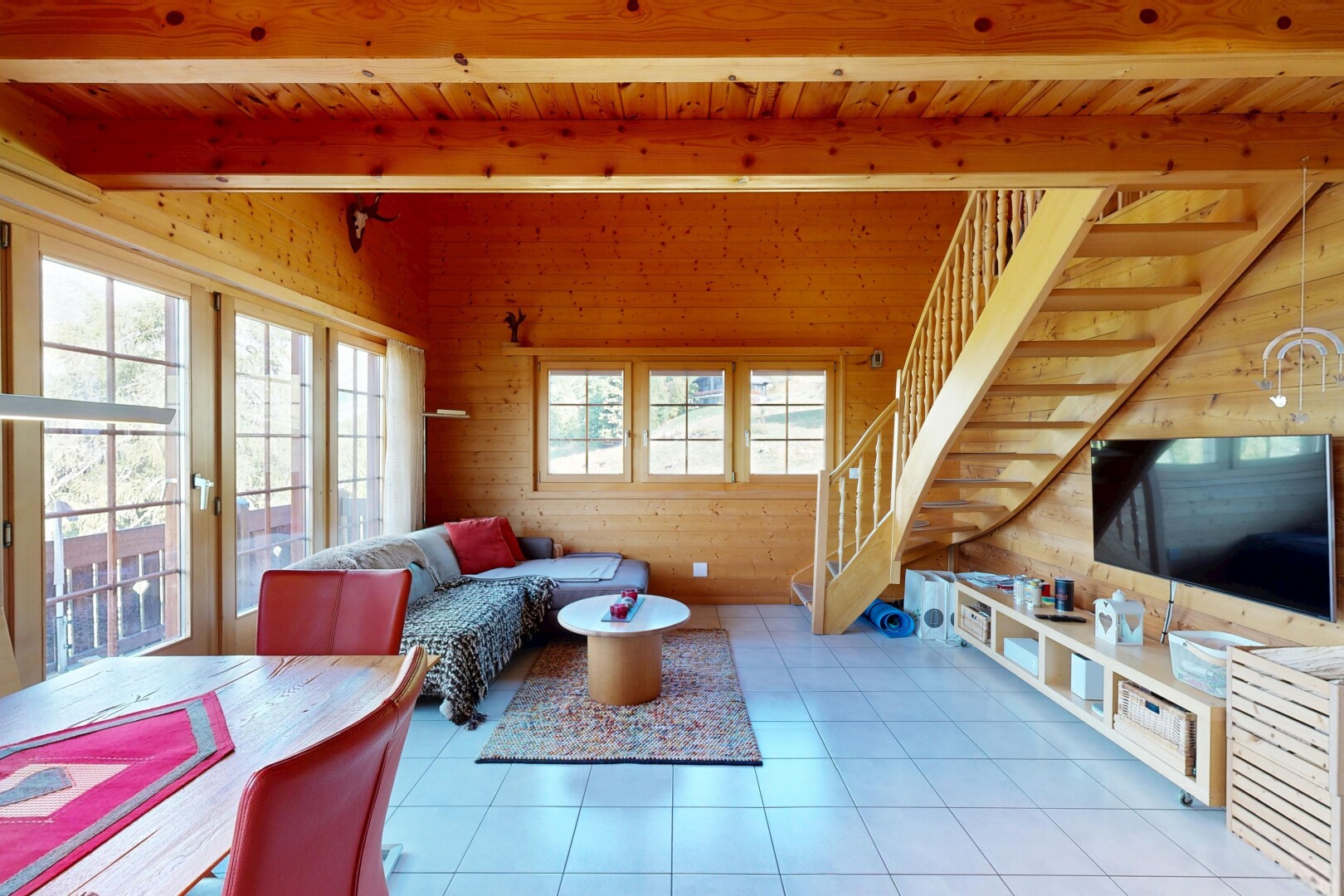 salon / salle à manger avec escaliers, télévision, plafond à poutres, beamed ceiling, et mur en bois