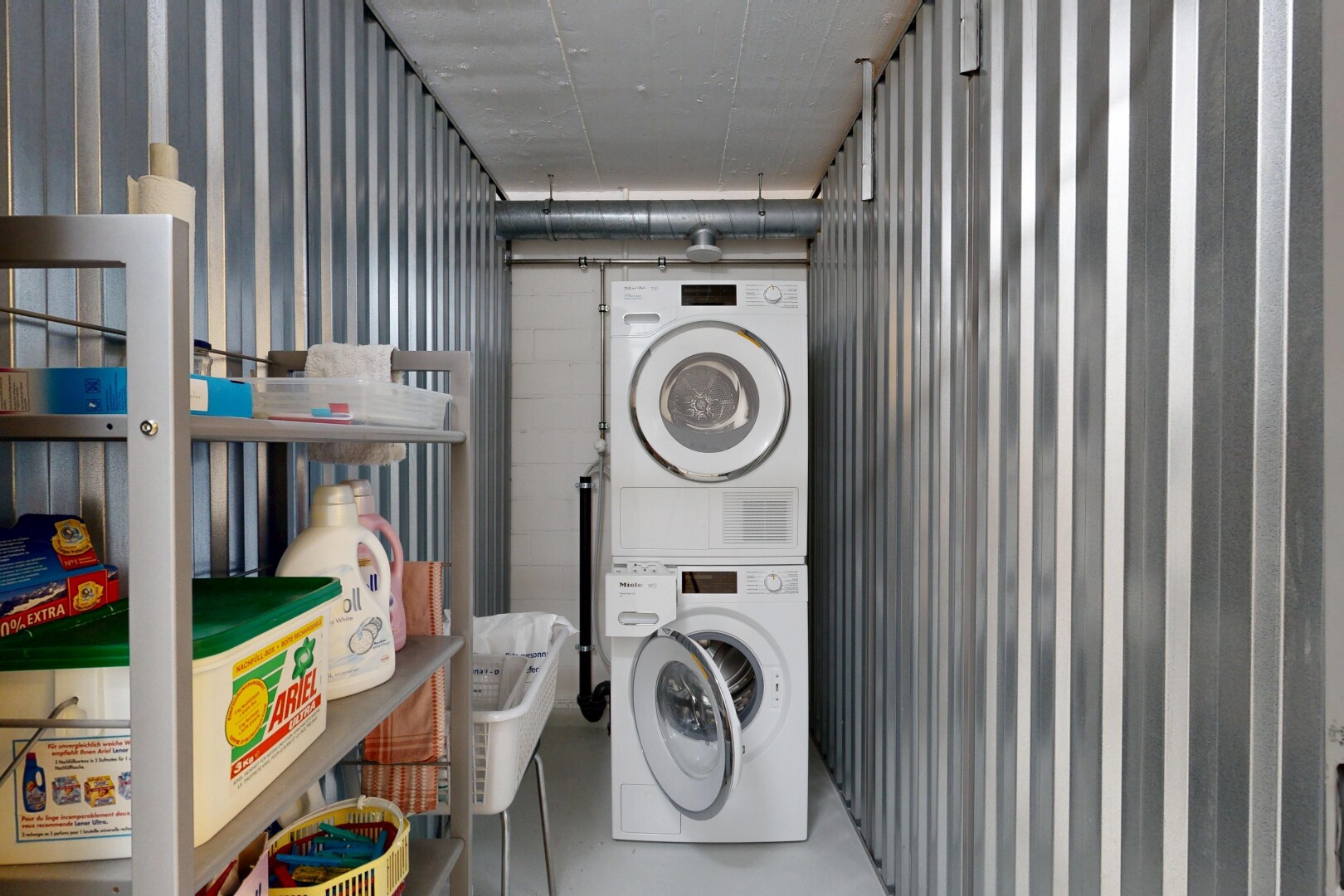 buanderie avec buanderie, inside community, concrete floor, lave-linge et sèche-linge superposés, et mur en métal