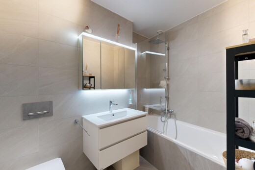 salle de bains avec lavabo (ou coiffeuse selon le contexte), salle de bain complète, douche-bain combinés, miroir, et mur en carrelage