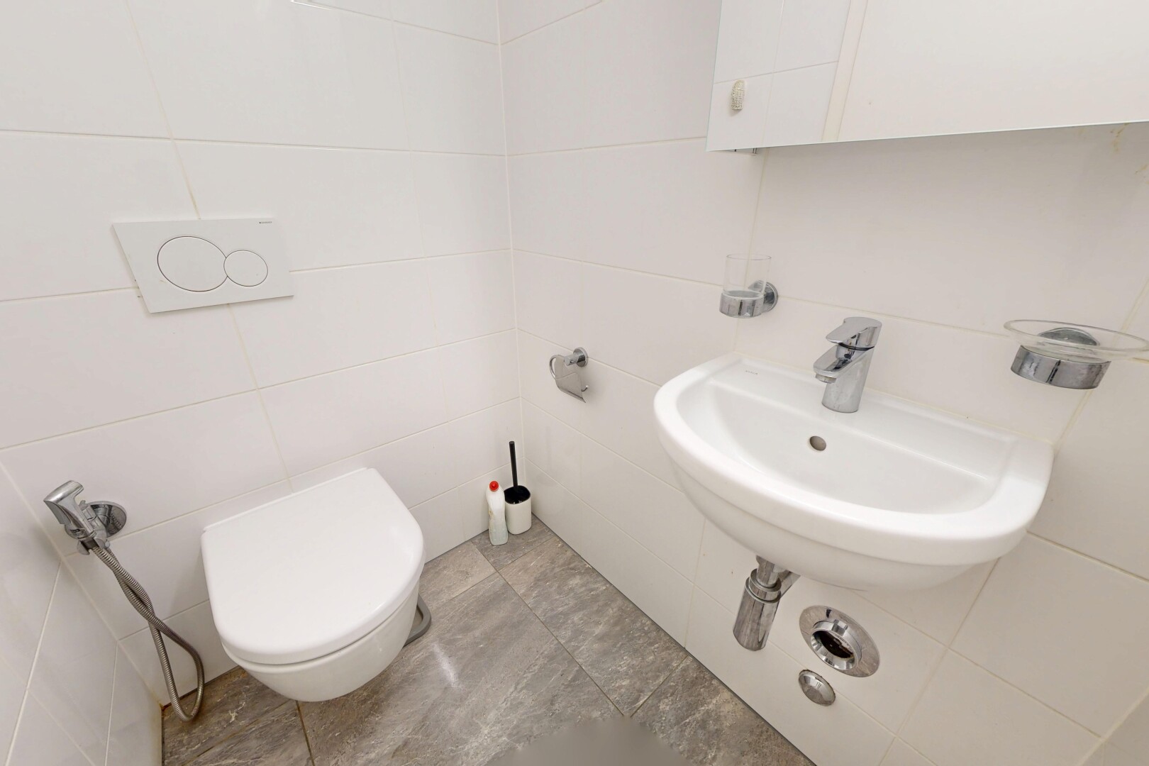 salle de bains avec mur en carrelage, tile wall, light floor, évier, et toilette