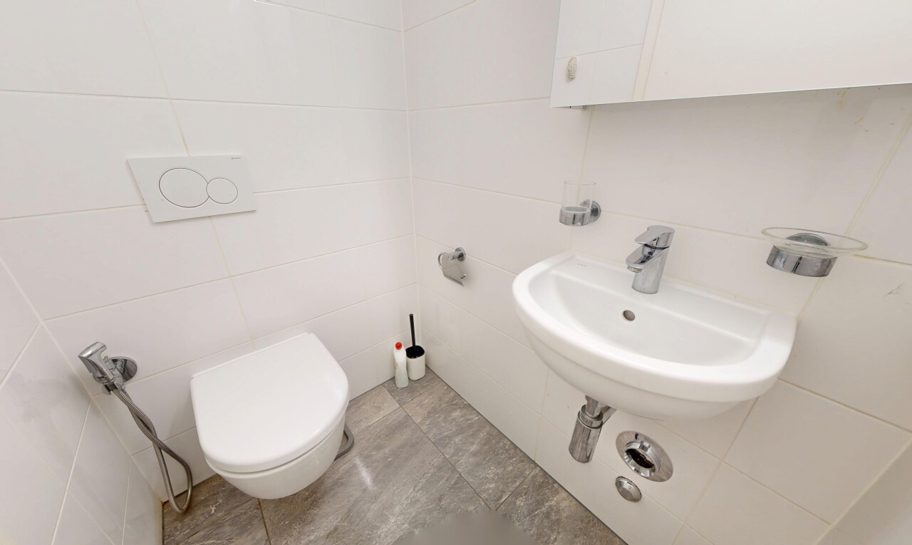salle de bains avec mur en carrelage, tile wall, light floor, évier, et toilette