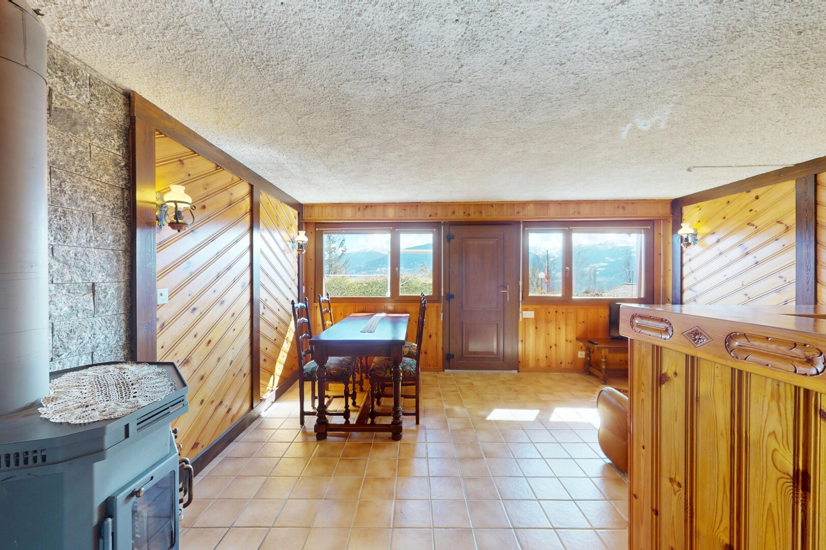 salle à manger avec lumière naturelle, mur en bois, poêle à bois, bar intérieur, et plafond texturé