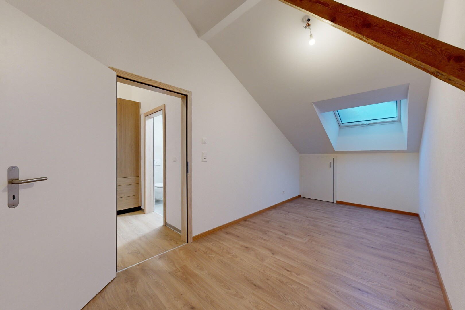 pièce vide avec plafond voûté, plancher de bois, poutres apparentes, et lucarne