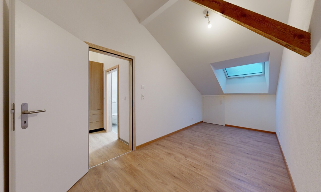 pièce vide avec plafond voûté, poutres apparentes, lucarne, et plancher de bois