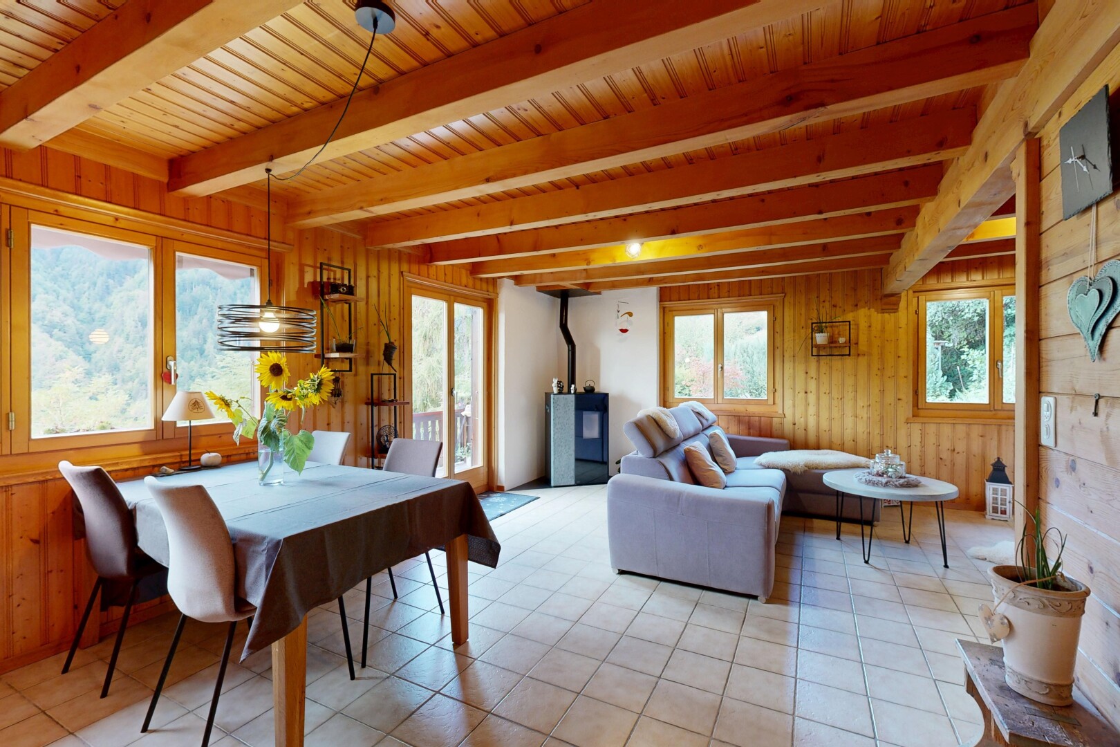 salon / salle à manger avec poêle à bois, plafond à poutres, beamed ceiling, high end ceiling, et dated wood wall