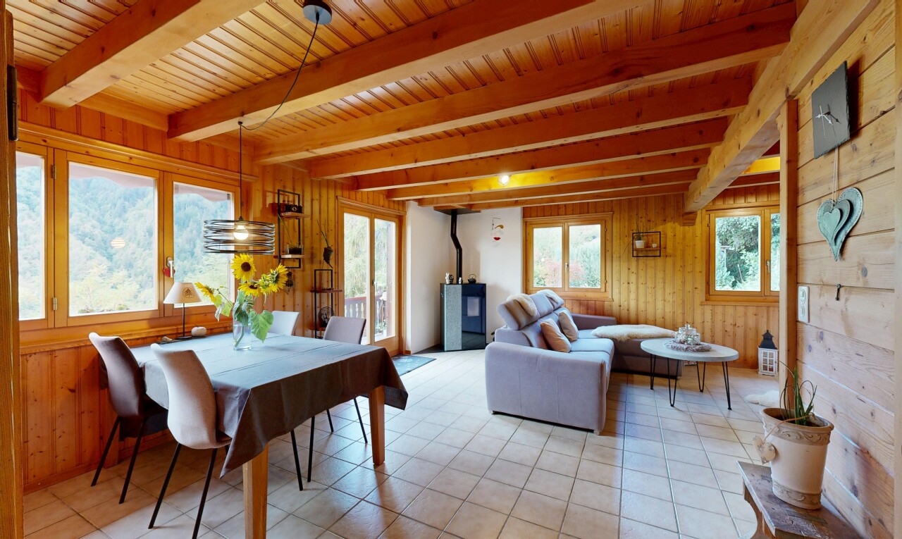 salon / salle à manger avec poêle à bois, plafond à poutres, beamed ceiling, high end ceiling, et dated wood wall