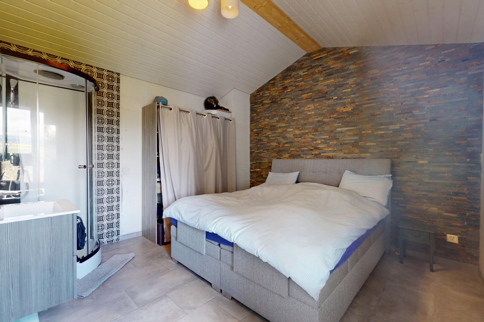 chambre avec plafond voûté, plafond à poutres, mur en pierre, lumière naturelle, et ventilateur de plafond