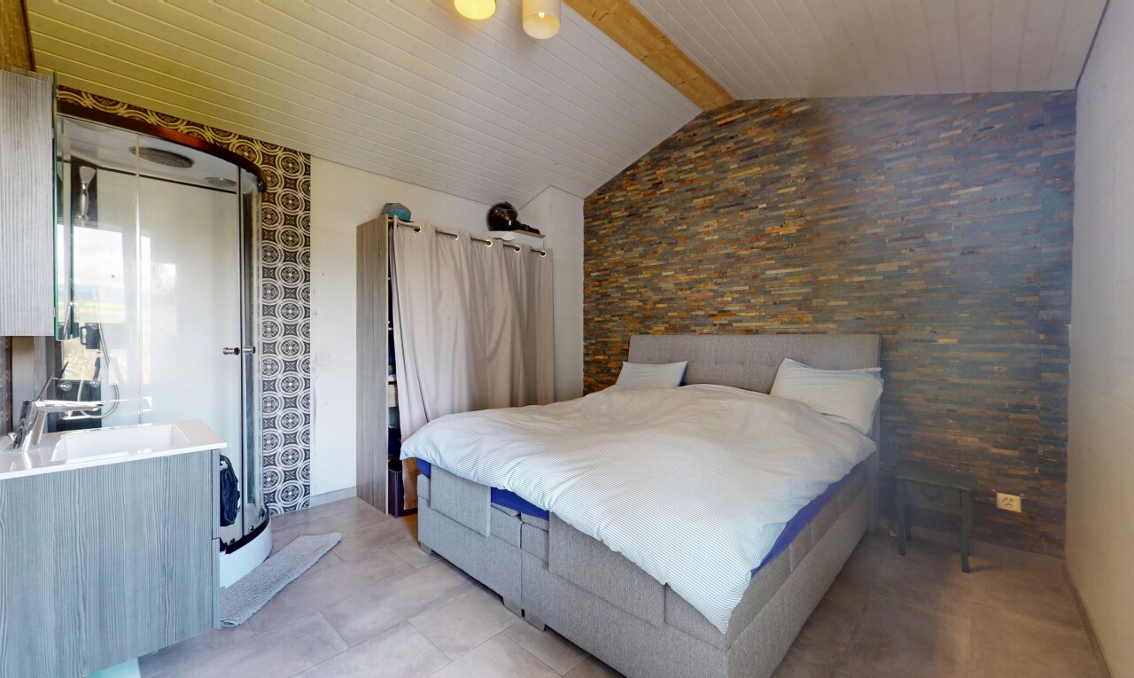 chambre avec plafond voûté, plafond à poutres, mur en pierre, lumière naturelle, et ventilateur de plafond