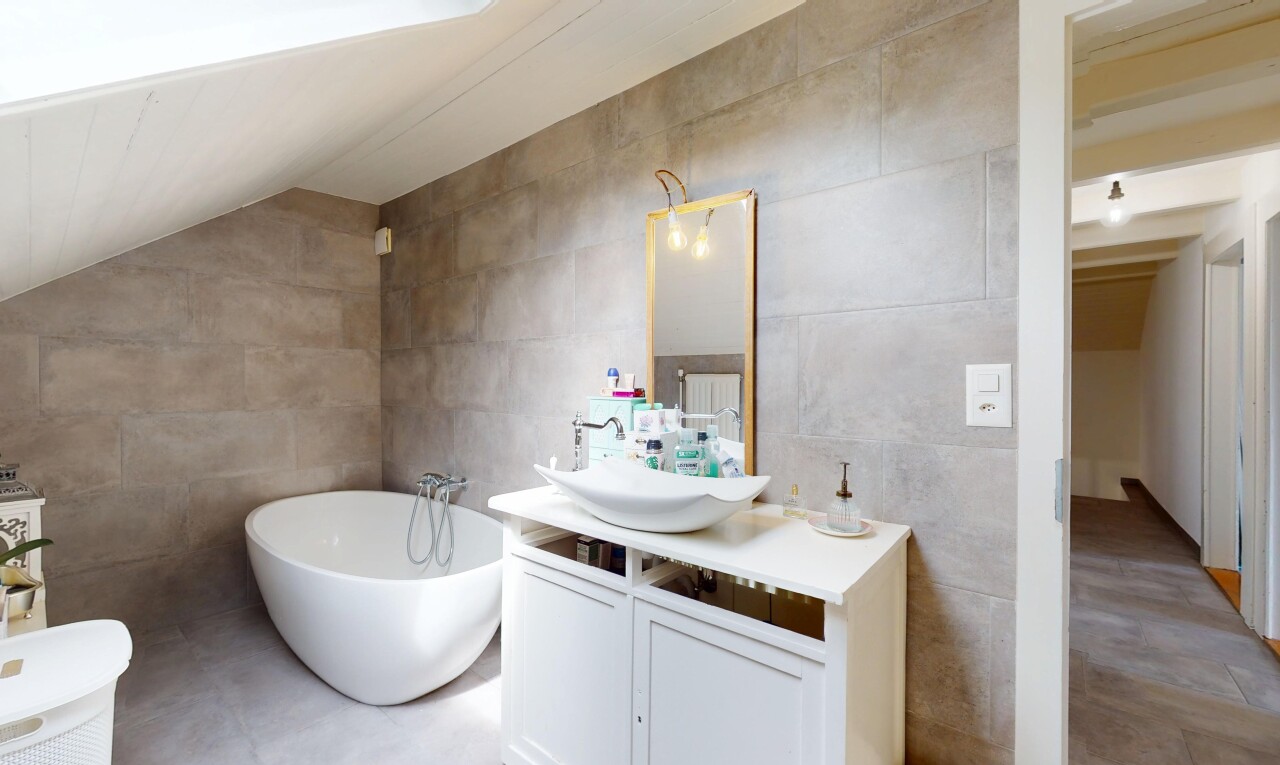 salle de bains avec lavabo (ou coiffeuse selon le contexte), évier, bain, mur en carrelage, et miroir
