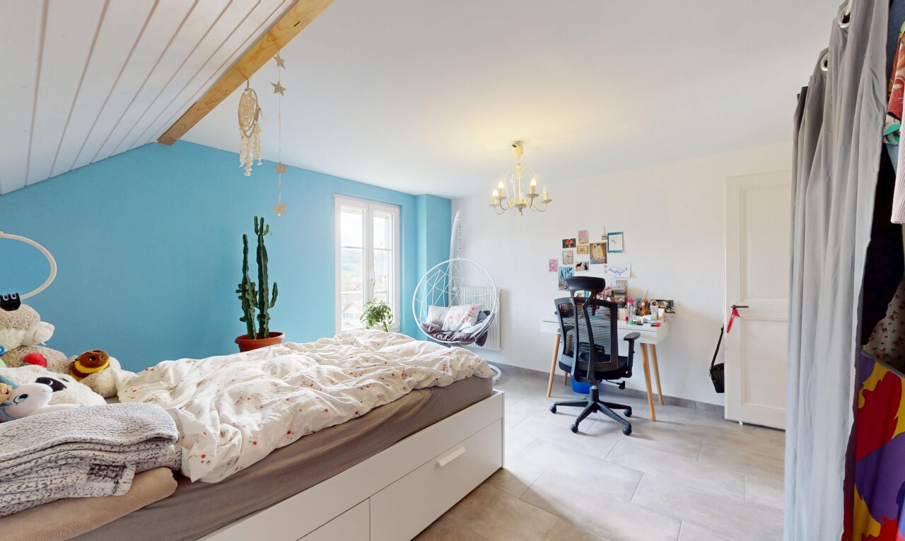 chambre avec plafond à poutres, lumière naturelle, espace bureau, lustre remarquable, et cloison sèche