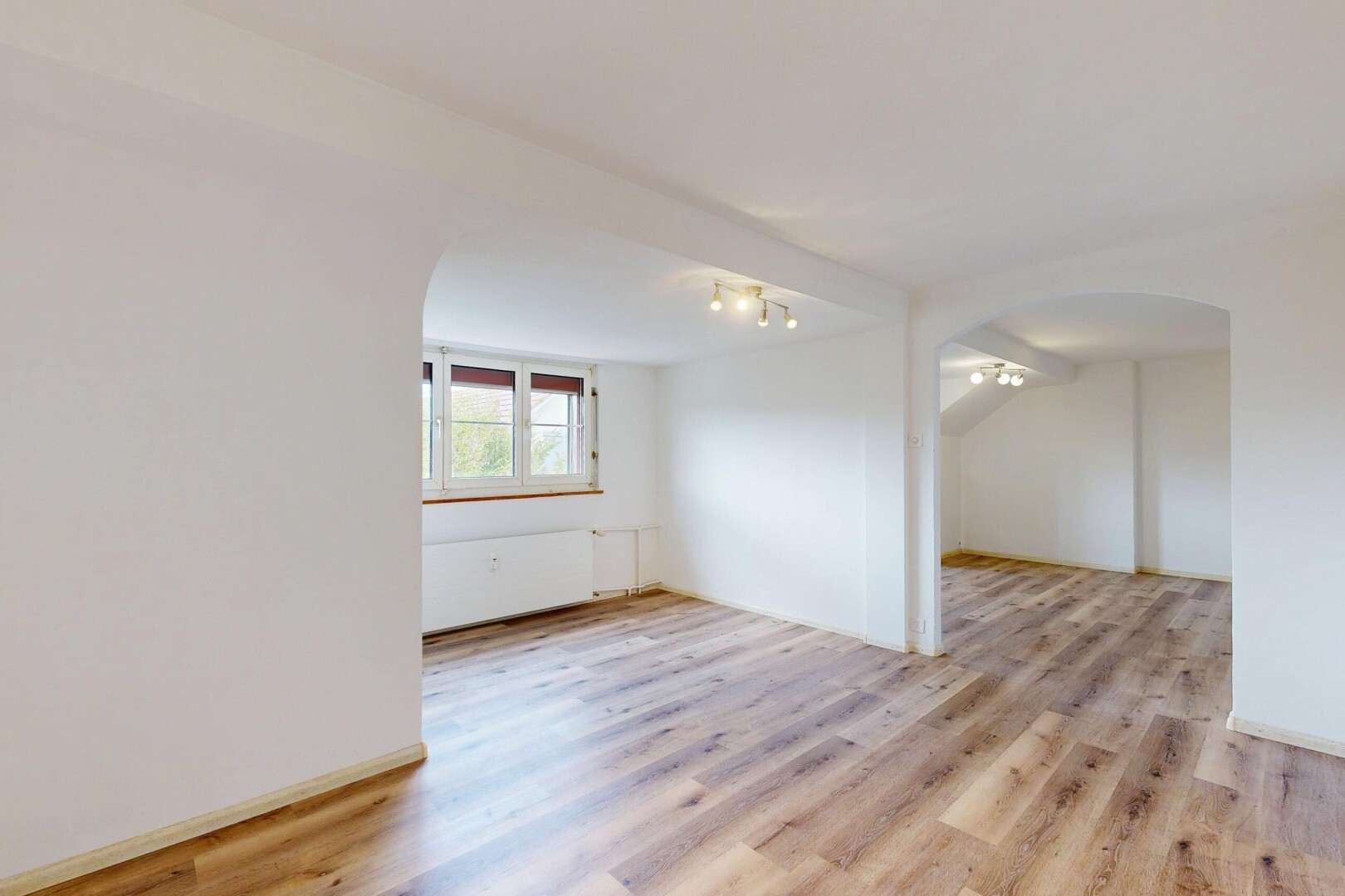 unfurnished room with track lighting, arched walkways, and light wood-style floors