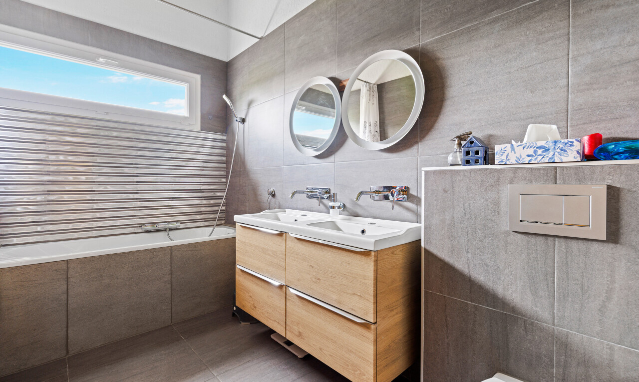 full bath with tile walls, tiled shower / bath, double vanity, and dark tile patterned flooring
