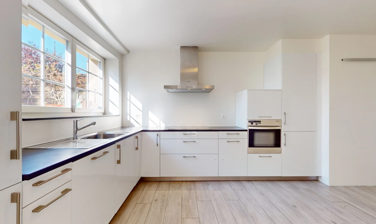 cuisine avec hotte, four, meubles blancs, lumière naturelle, et plancher de bois