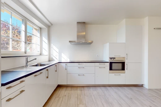 cuisine avec hotte, four, meubles blancs, lumière naturelle, et plancher de bois