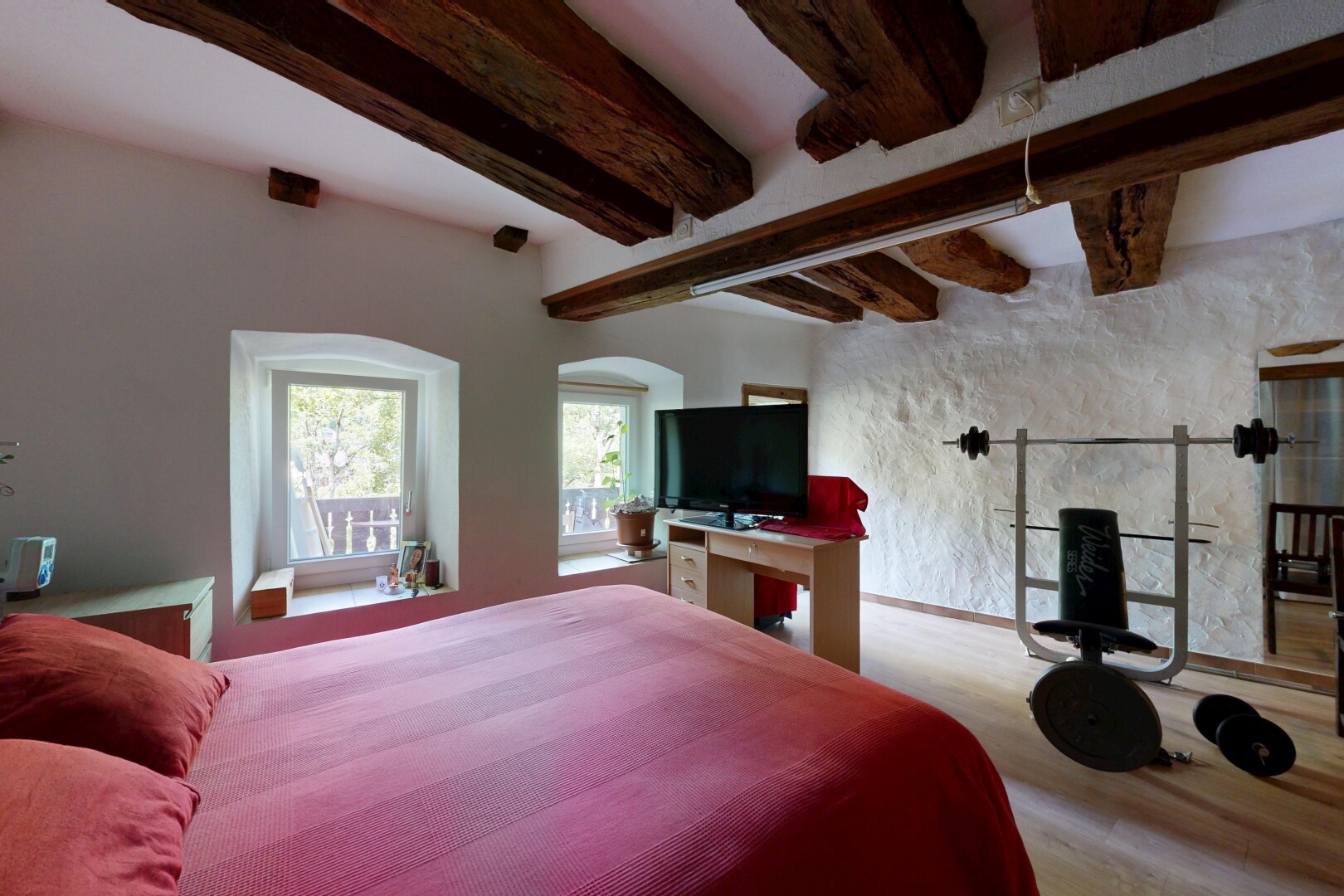 room / bedroom with beam ceiling, a barn door, and wood finished floors