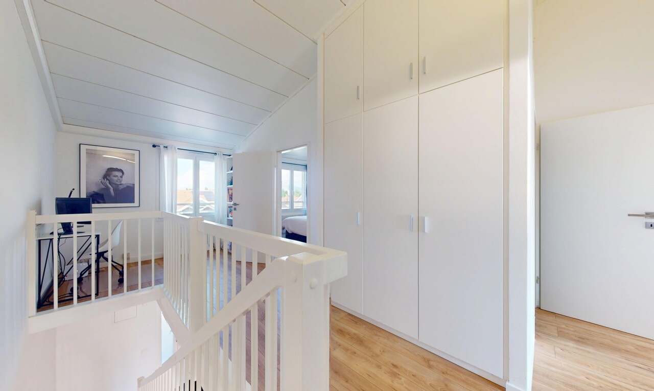 corridor with an upstairs landing, light wood-style flooring, and lofted ceiling