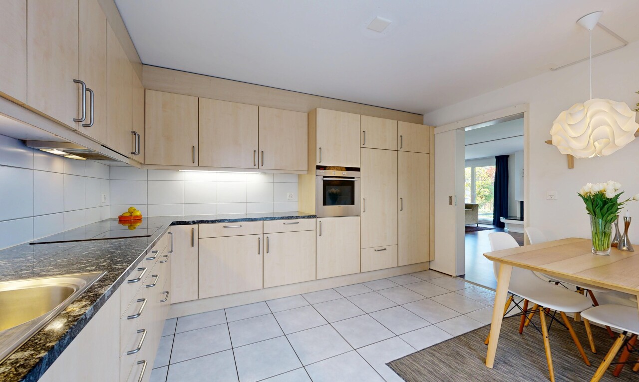 kitchen featuring light wood finish cabinetry, decorative backsplash, stainless steel oven, and hanging light fixtures