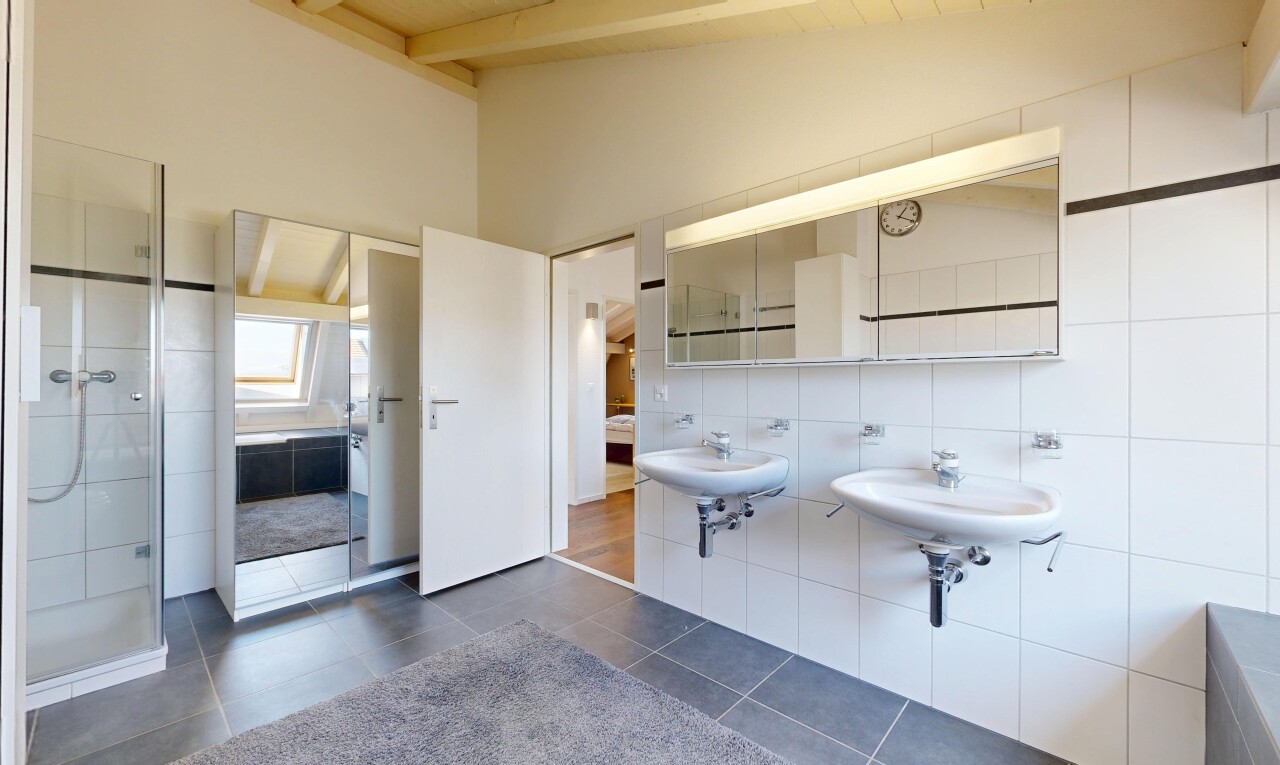 bathroom with two sinks, lofted ceiling, a shower stall, dark tile patterned flooring, and tile walls