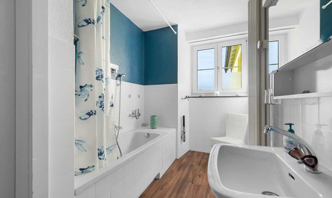 salle de bains avec sol en finition bois, évier, lumière naturelle, et salle de bain complète