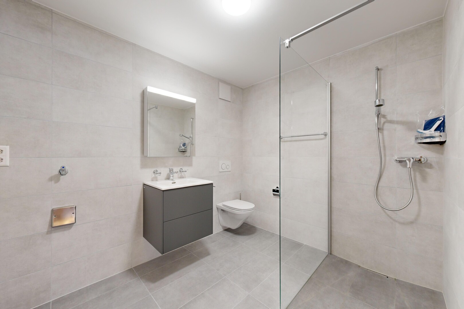 salle de bains avec mur carrelé, toilettes, meuble-lavabo, miroir, et douche