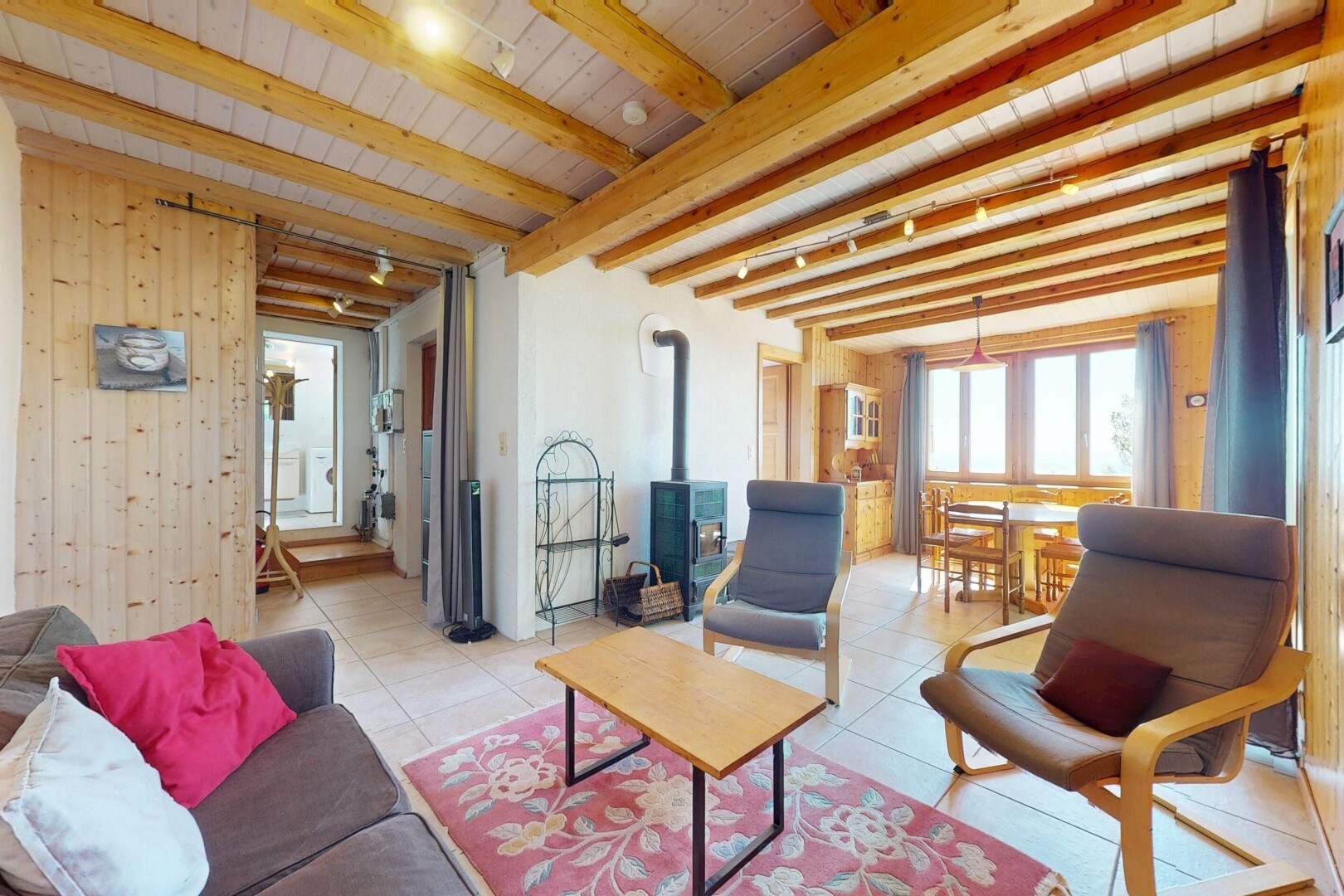 living / dining room with wooden walls, light tile patterned flooring, a wood stove, wooden ceiling, and beamed ceiling