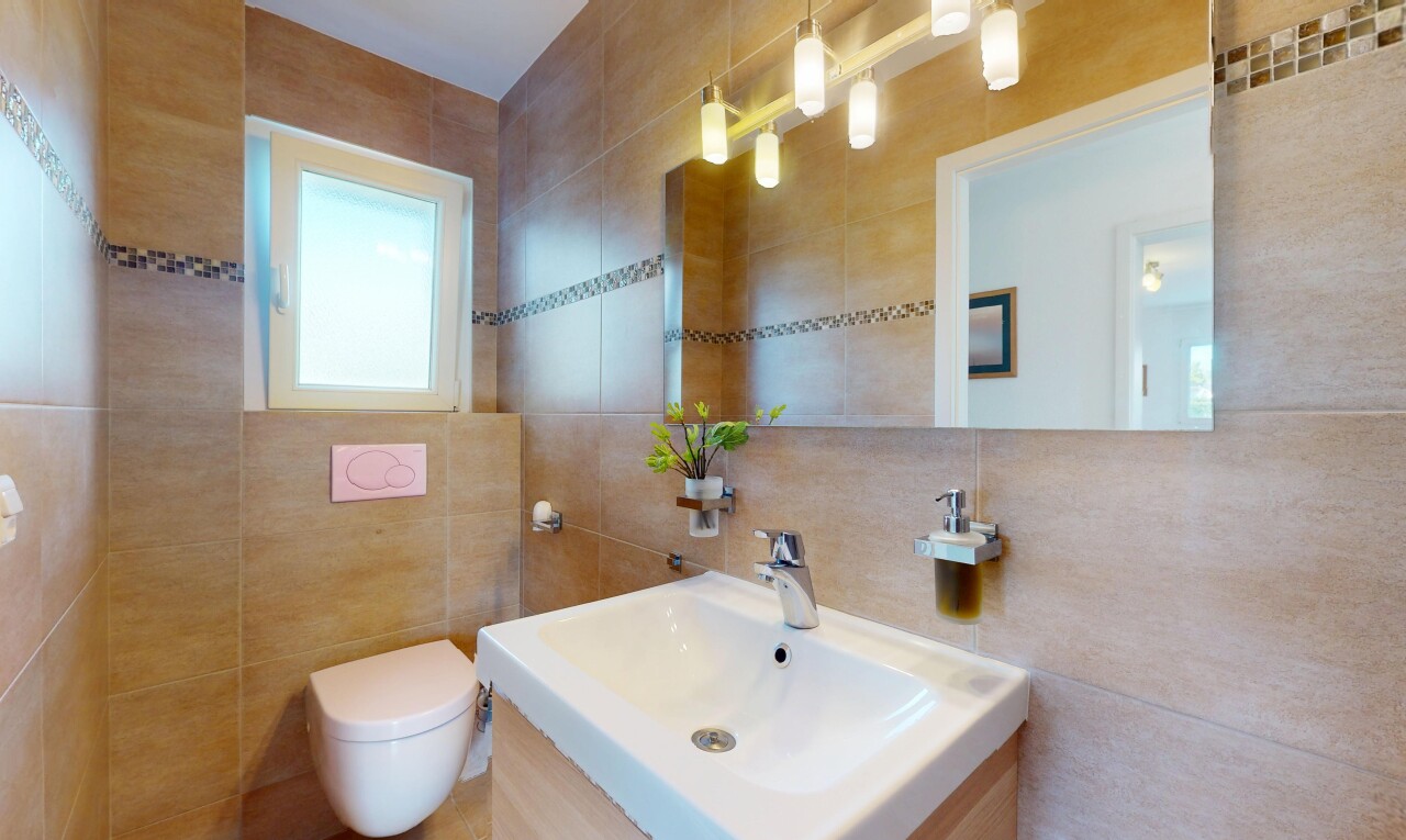 salle de bains avec miroir, mur en carrelage, lumière naturelle, toilette, et évier