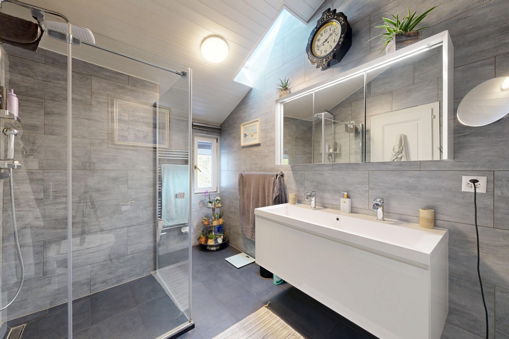 full bath featuring tile walls, double vanity, a shower stall, and lofted ceiling