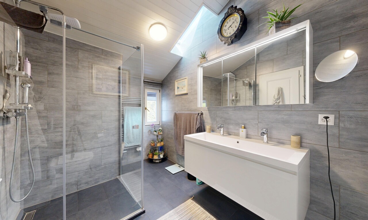 full bath featuring tile walls, double vanity, a shower stall, and lofted ceiling