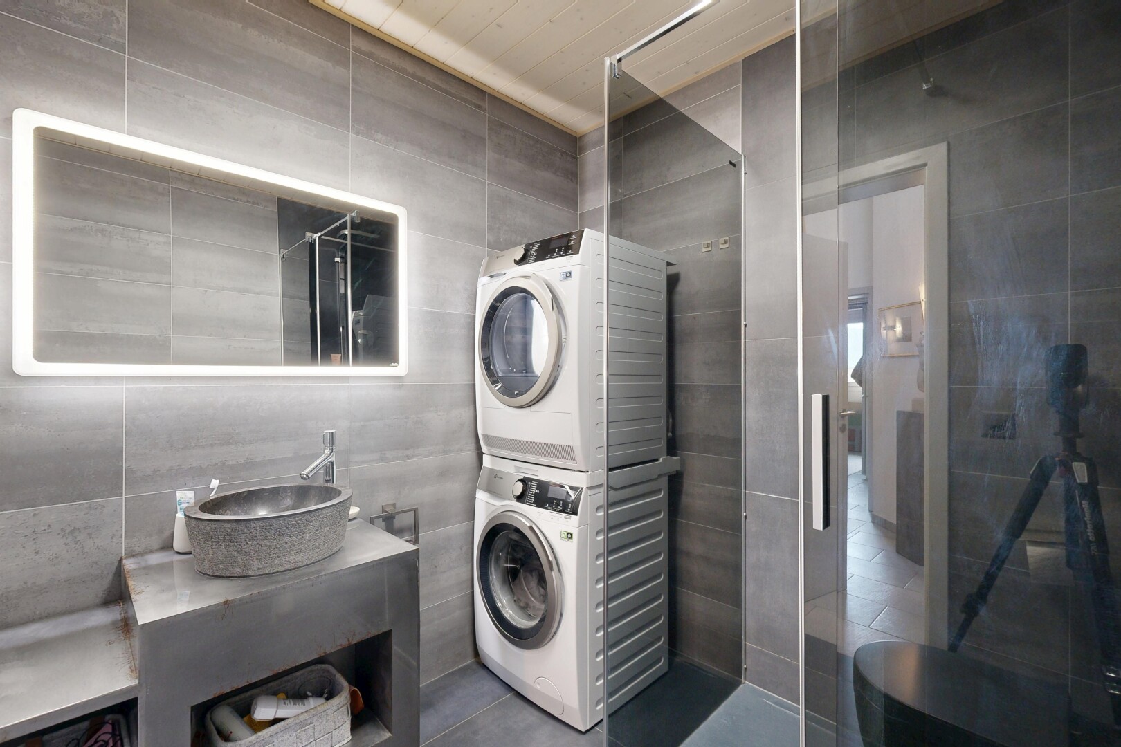salle de bains avec mur en carrelage, tile wall, lavabo (ou coiffeuse selon le contexte), miroir, et lave-linge et sèche-linge superposés