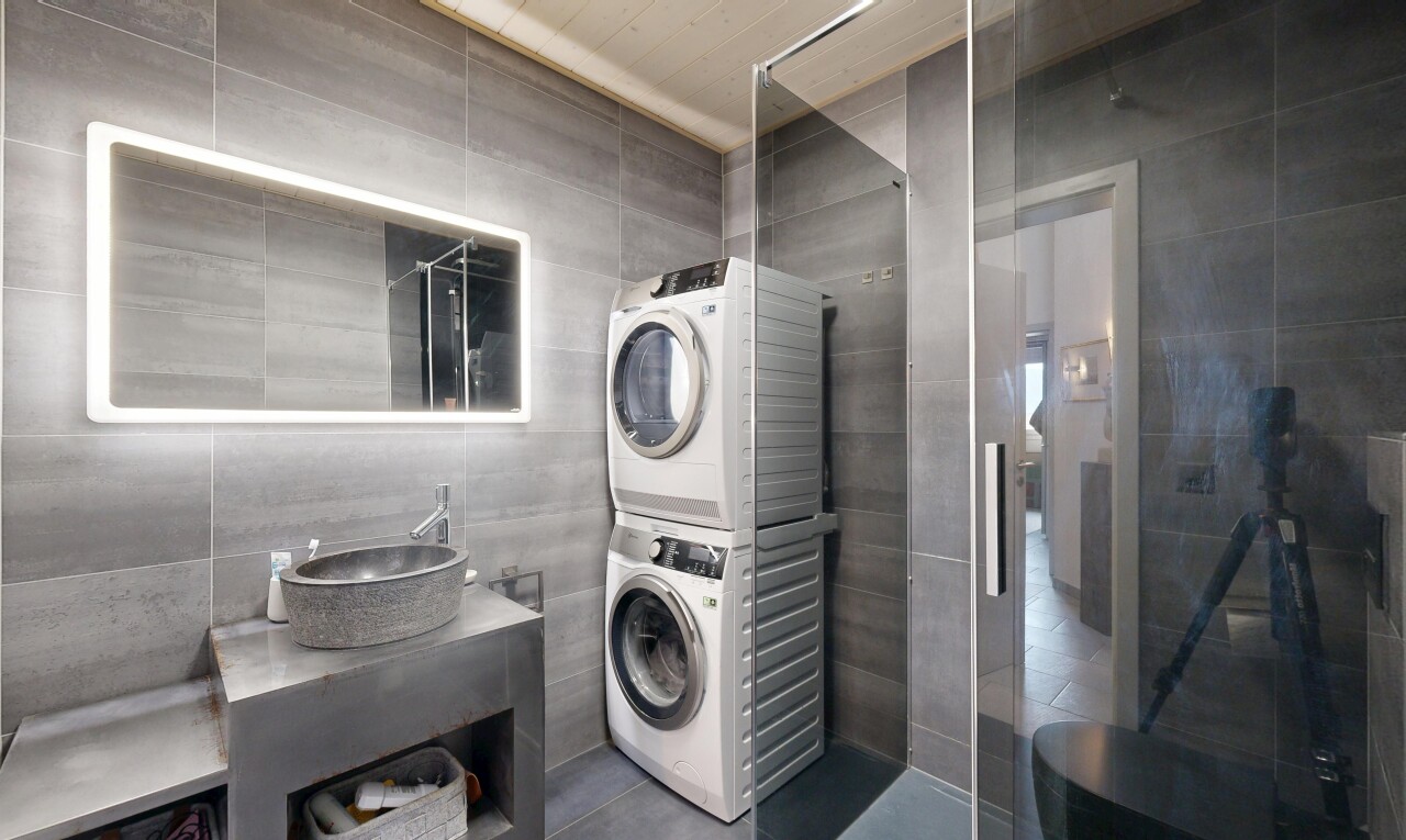 salle de bains avec mur en carrelage, tile wall, lavabo (ou coiffeuse selon le contexte), miroir, et lave-linge et sèche-linge superposés