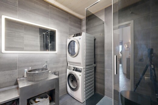 salle de bains avec mur en carrelage, tile wall, lavabo (ou coiffeuse selon le contexte), miroir, et lave-linge et sèche-linge superposés