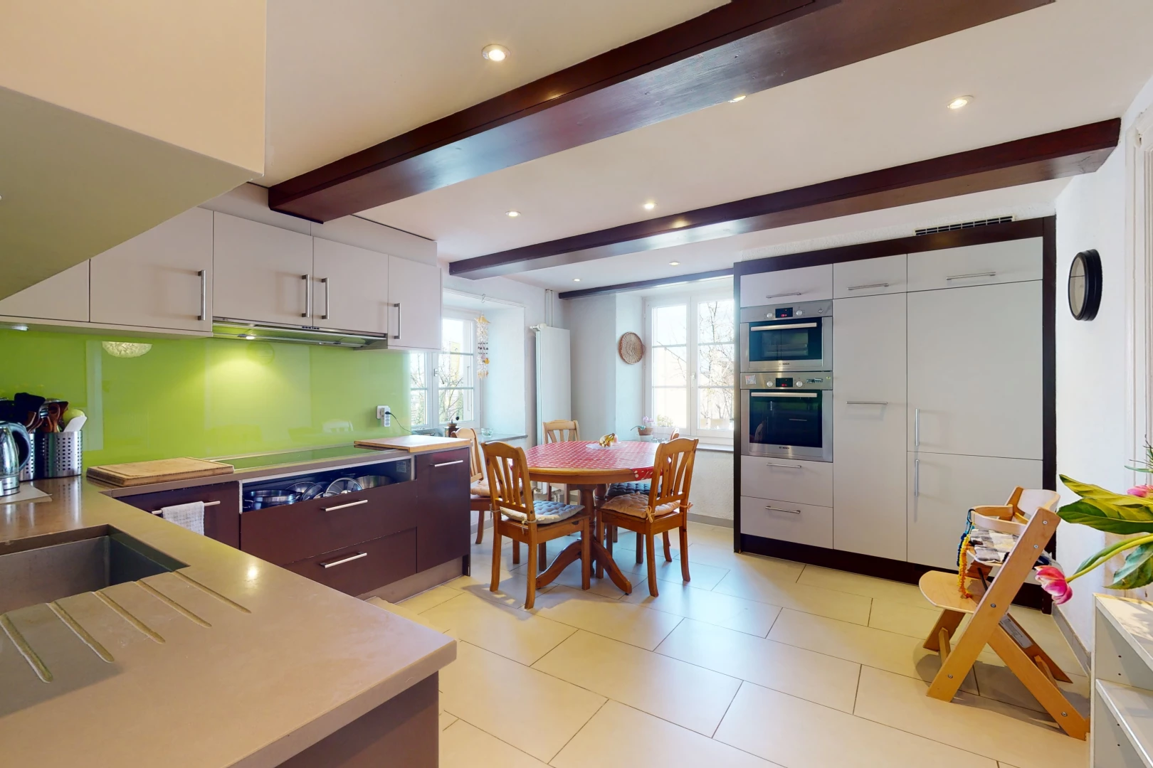 cuisine avec poutres apparentes, lumière naturelle, acier inoxydable, carrelage, four, meubles blancs, plan de travail clair, et sol clair