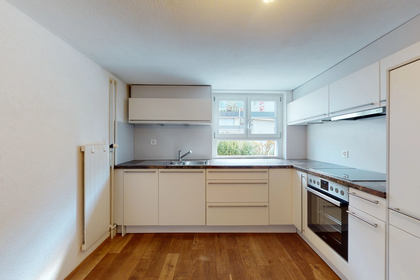 cuisine avec parquet, lumière naturelle, four, hotte, cuisinière électrique, meubles blancs, et sol clair
