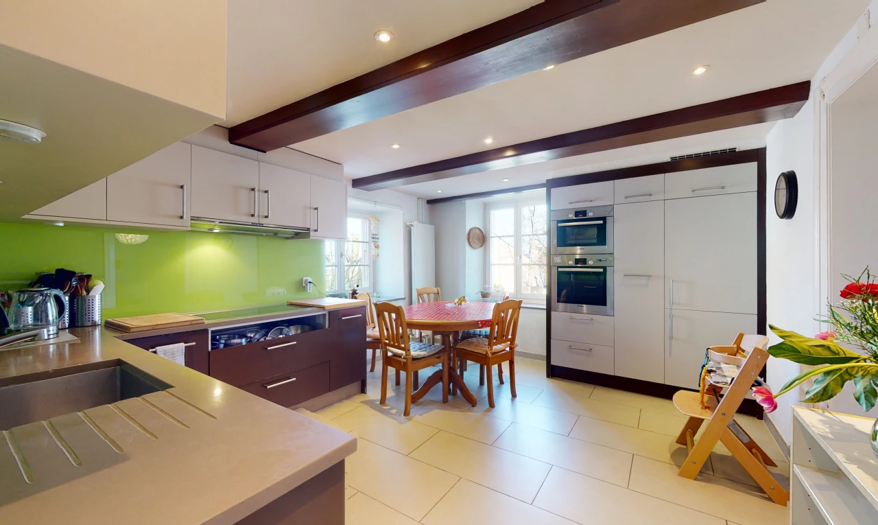 cuisine avec poutres apparentes, lumière naturelle, acier inoxydable, carrelage, four, meubles blancs, plan de travail clair, et sol clair