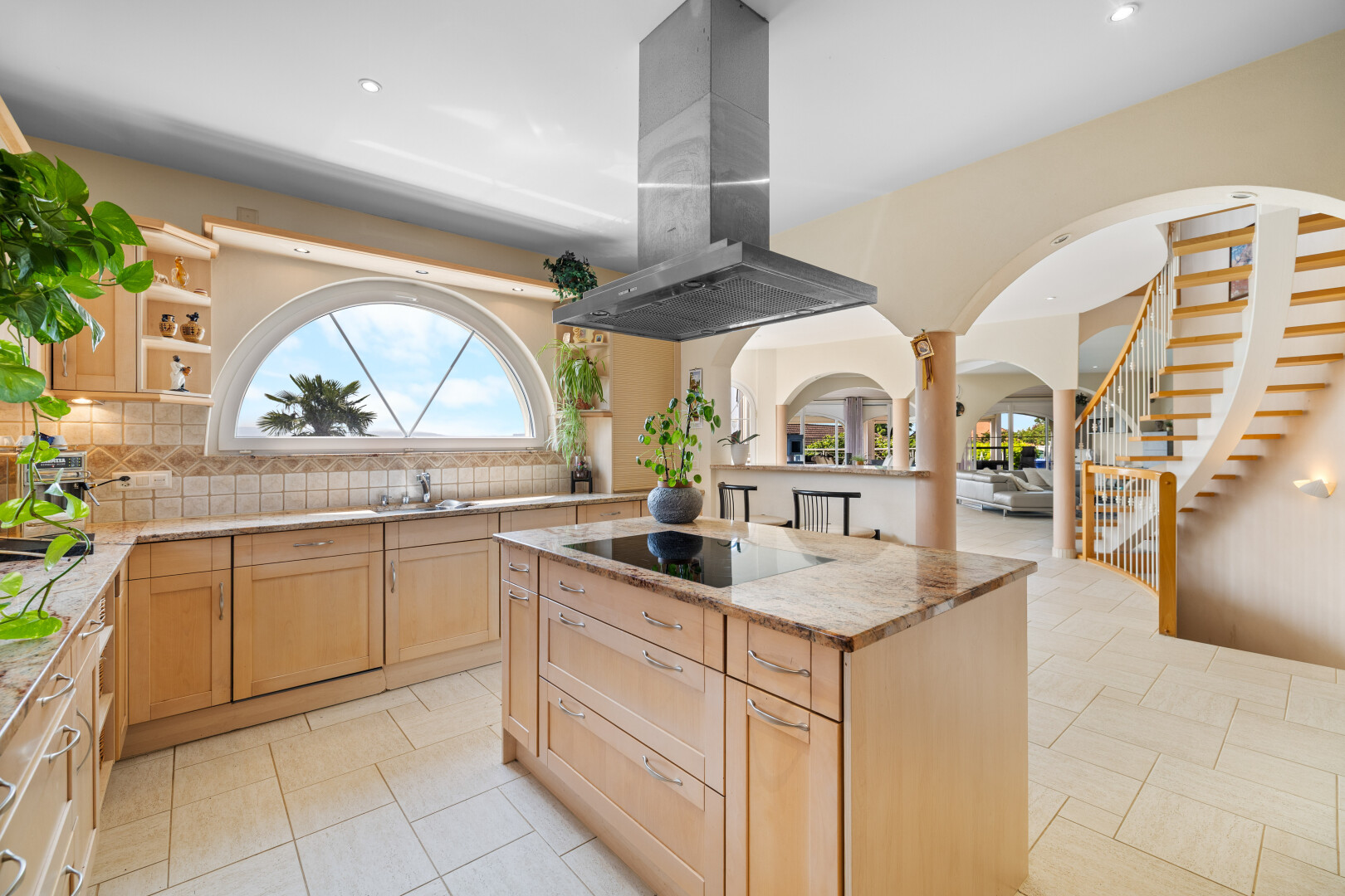 kitchen featuring light brown cabinetry, island exhaust hood, tasteful backsplash, arched walkways, and light stone countertops