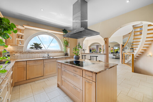 kitchen featuring light brown cabinetry, island exhaust hood, tasteful backsplash, arched walkways, and light stone countertops