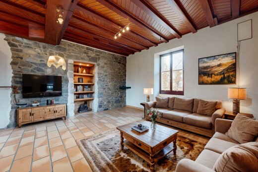 salon avec poutres apparentes, lumière naturelle, mur en pierre, plafond de bois, et télévision