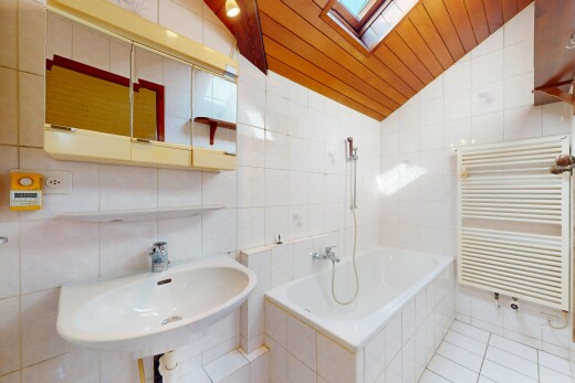 salle de bains avec mur carrelé, plafond voûté, baignoire, radiateur, et lucarne
