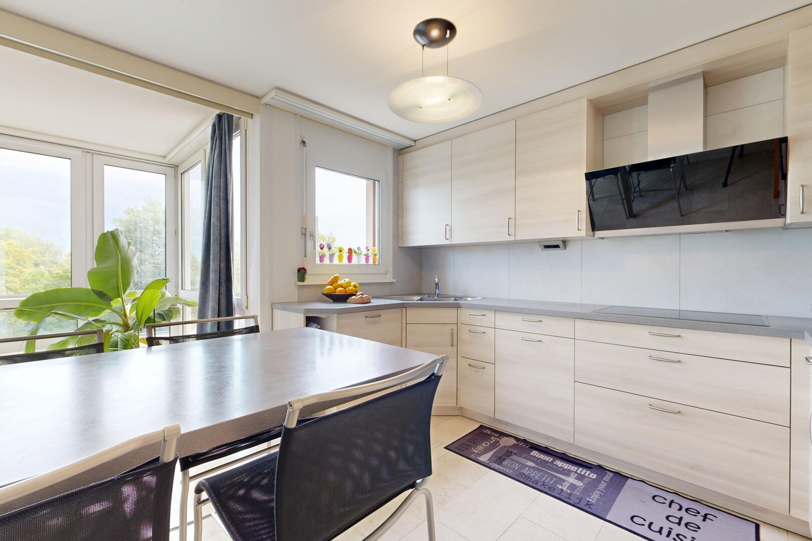 kitchen featuring ventilation hood, hanging light fixtures, stainless steel countertops, light wood finish cabinets, and black electric stovetop