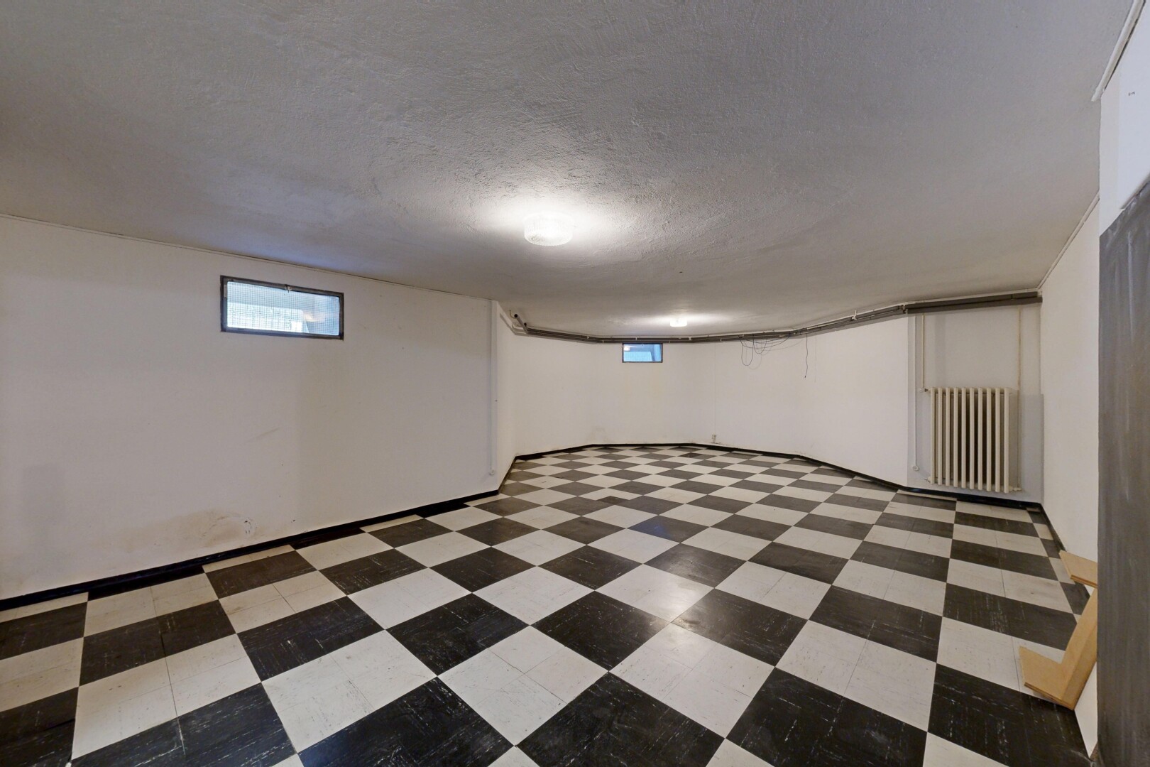 pièce vide avec radiateur, lumière naturelle, plafond texturé, sous-sol, et sol en vinyle