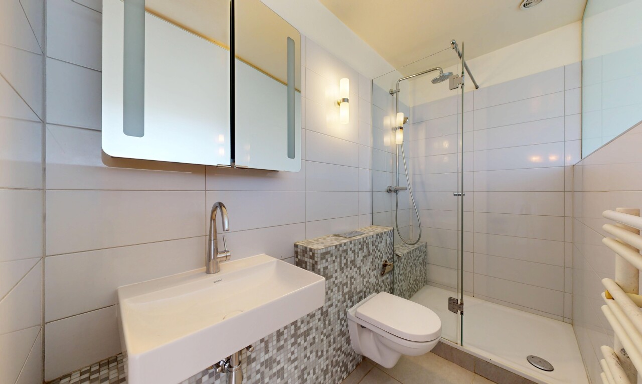 salle de bains avec évier, miroir, toilette, douche, et mur en carrelage