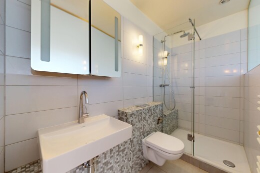 salle de bains avec évier, miroir, toilette, douche, et mur en carrelage